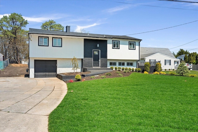 split foyer home featuring a front lawn, a garage, brick siding, driveway, and a chimney