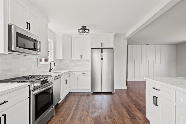 kitchen featuring a sink, dark wood-style flooring, decorative backsplash, light stone counters, and appliances with stainless steel finishes