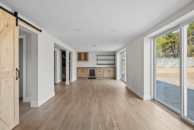unfurnished living room featuring a barn door, beverage cooler, light wood-style flooring, and baseboards