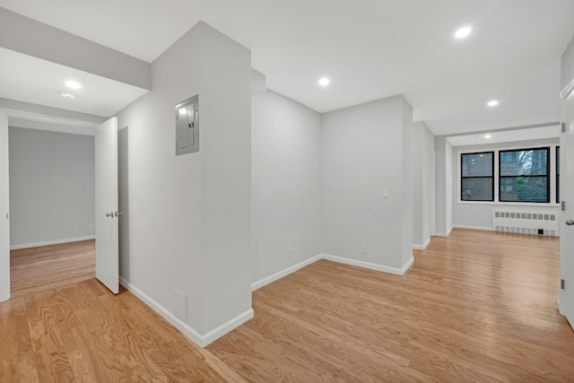 corridor featuring baseboards, radiator heating unit, light wood finished floors, and electric panel