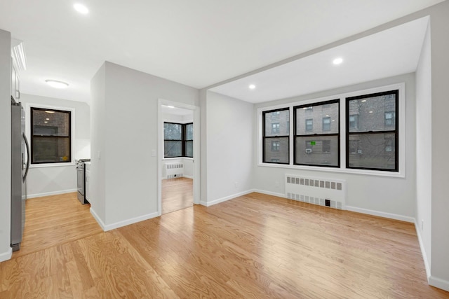 spare room featuring radiator, baseboards, and light wood-type flooring