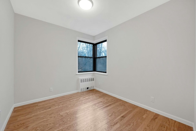 empty room featuring baseboards, light wood finished floors, and radiator