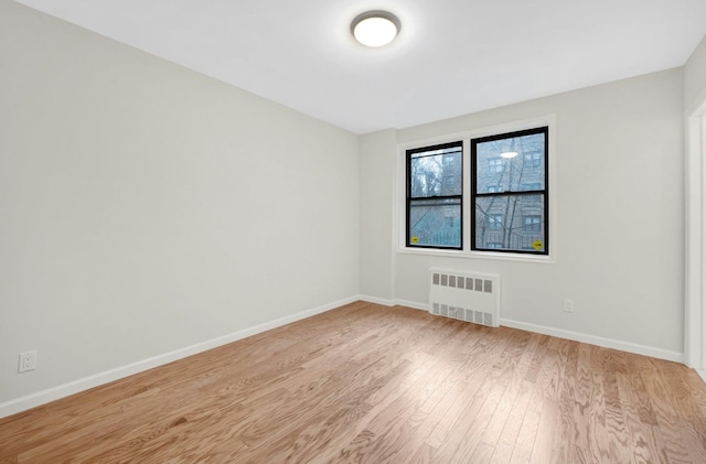 spare room with light wood-style floors, radiator, and baseboards
