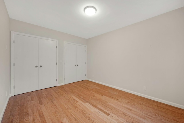 unfurnished bedroom featuring light wood-style floors, two closets, and baseboards