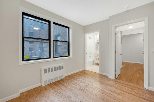unfurnished bedroom featuring light wood finished floors, radiator heating unit, and baseboards