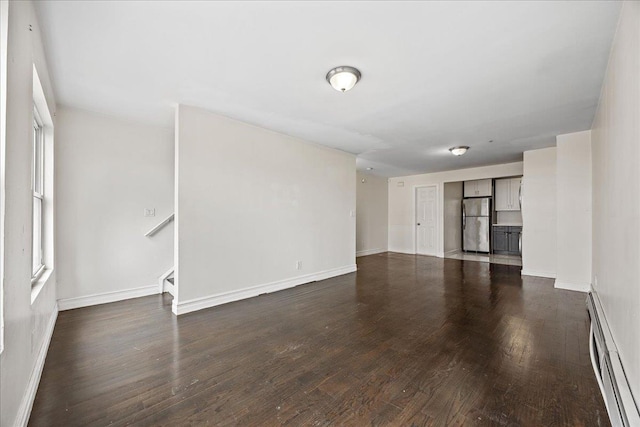 unfurnished living room with dark wood-style floors, a baseboard heating unit, stairway, and baseboards