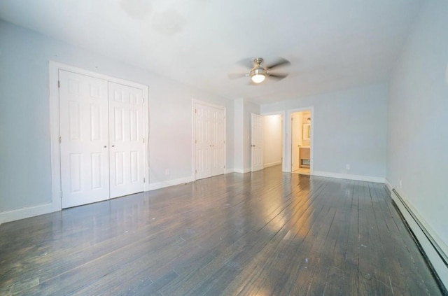 unfurnished bedroom featuring baseboards, two closets, baseboard heating, and wood-type flooring