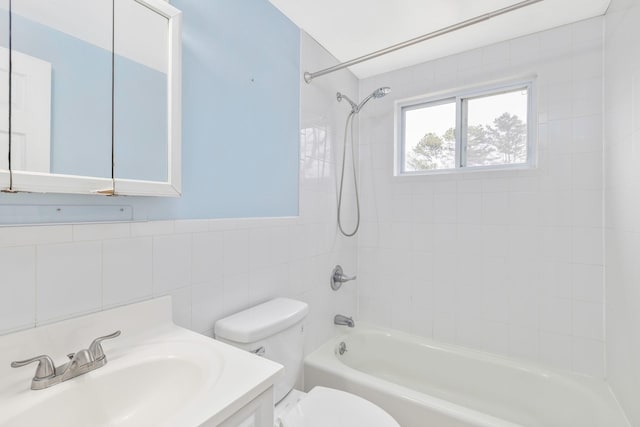 full bath featuring vanity, tile walls, toilet, tub / shower combination, and a wainscoted wall