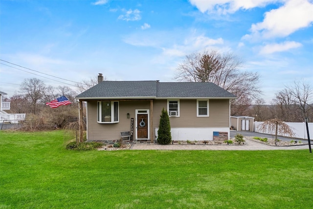 bi-level home with a chimney, fence, a shingled roof, a front lawn, and an outbuilding