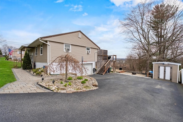 view of home's exterior with a storage unit, an outbuilding, an attached garage, stairway, and aphalt driveway