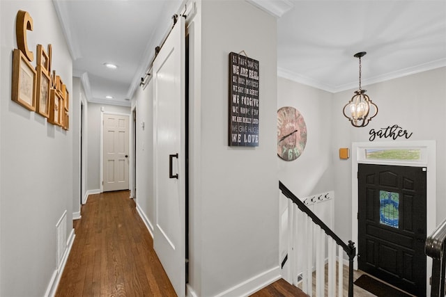 foyer entrance featuring a barn door, visible vents, dark wood-type flooring, crown molding, and a notable chandelier