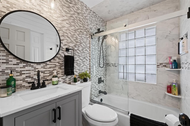 bathroom featuring toilet, vanity, tile walls, bath / shower combo with glass door, and tasteful backsplash