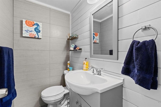 half bathroom with tile walls, vanity, ornamental molding, and toilet
