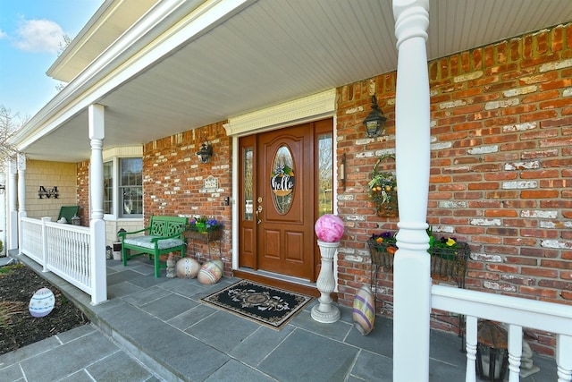 view of exterior entry with a porch and brick siding
