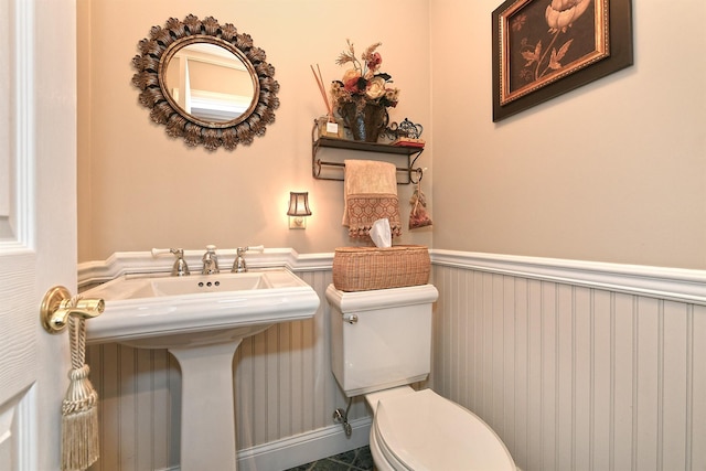 half bath featuring a sink, toilet, and a wainscoted wall