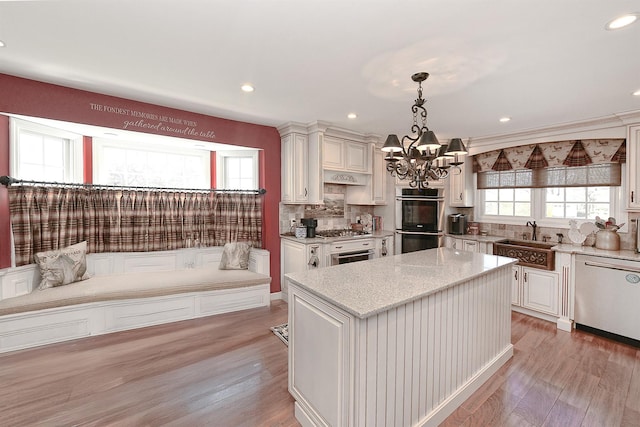 kitchen with a sink, stainless steel appliances, light wood-type flooring, decorative backsplash, and a chandelier