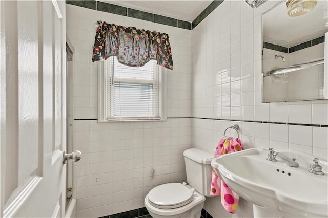 bathroom with a sink, tile walls, and toilet