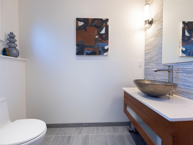 half bathroom featuring vanity, baseboards, tile patterned floors, toilet, and decorative backsplash
