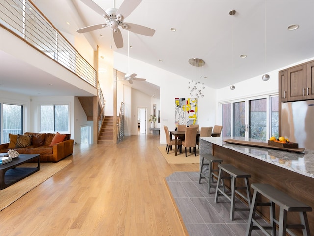 kitchen with ceiling fan, light wood-style flooring, stainless steel refrigerator, open floor plan, and a breakfast bar area
