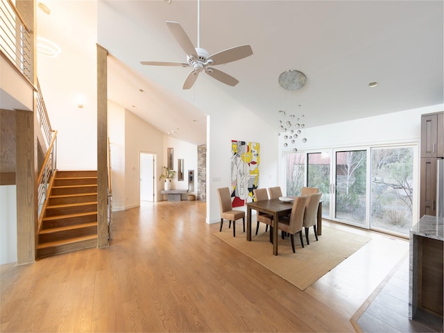 dining space with light wood finished floors, high vaulted ceiling, ceiling fan, and stairway