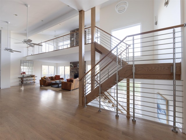 staircase featuring wood finished floors, ceiling fan, a high ceiling, and a fireplace