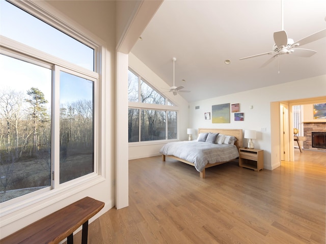 bedroom featuring light wood-style flooring, a ceiling fan, lofted ceiling, and a stone fireplace