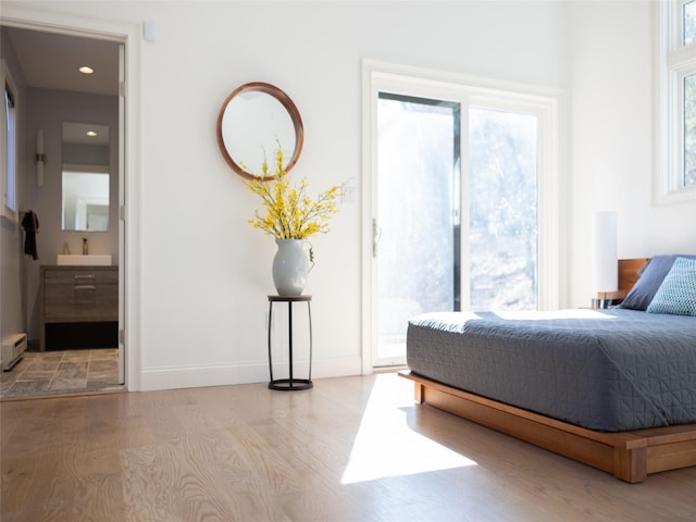 bedroom with ensuite bath, access to exterior, wood finished floors, a baseboard radiator, and baseboards