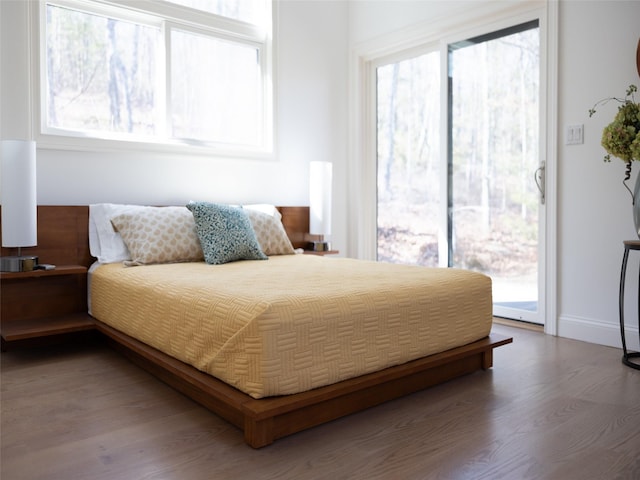 bedroom featuring access to outside, baseboards, multiple windows, and wood finished floors