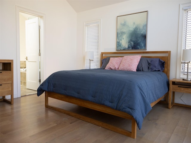 bedroom featuring wood finished floors, lofted ceiling, and connected bathroom