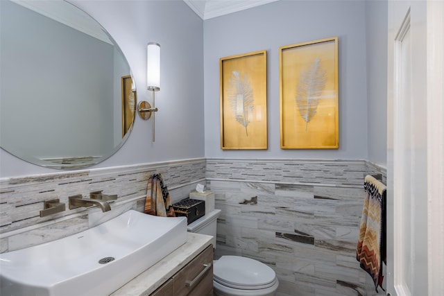 half bathroom with crown molding, vanity, toilet, wainscoting, and tile walls