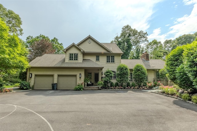 traditional home with a garage, driveway, a chimney, and a shingled roof