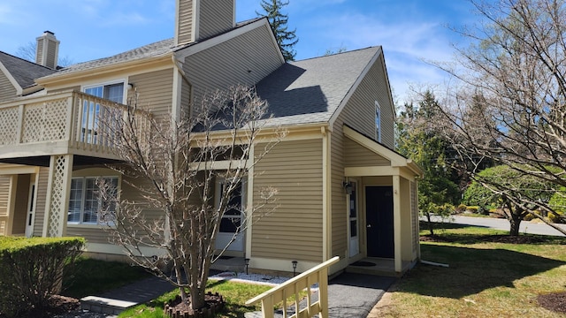 view of side of home with a yard, roof with shingles, and a chimney