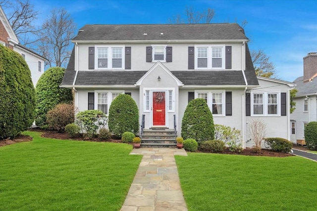 dutch colonial with roof with shingles, stucco siding, and a front yard