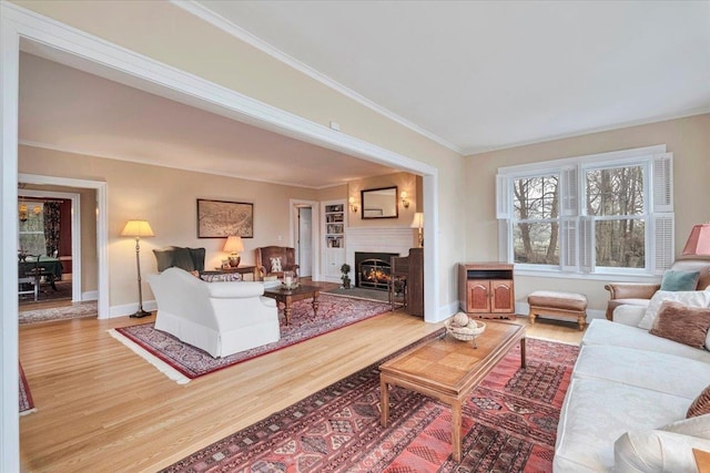 living area with baseboards, a lit fireplace, ornamental molding, and wood finished floors