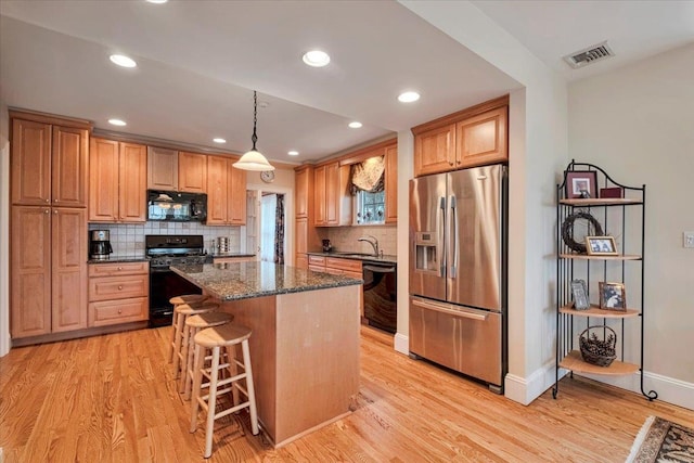 kitchen with light wood finished floors, a center island, tasteful backsplash, visible vents, and black appliances