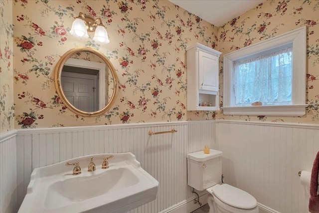 bathroom with a sink, a wainscoted wall, wallpapered walls, and toilet