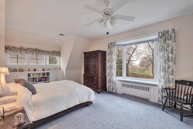carpeted bedroom with ceiling fan, visible vents, multiple windows, and radiator heating unit