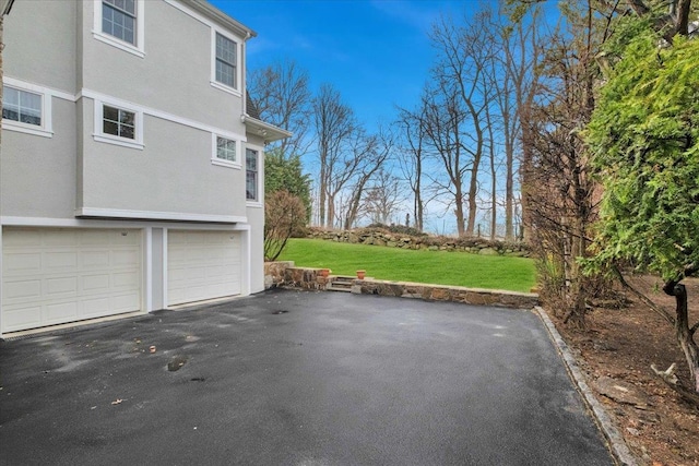 view of home's exterior with a lawn, a garage, aphalt driveway, and stucco siding