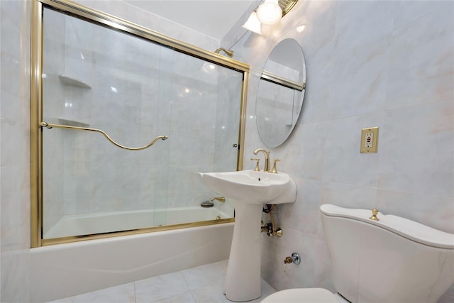 full bath featuring toilet, bath / shower combo with glass door, tile patterned floors, and tile walls