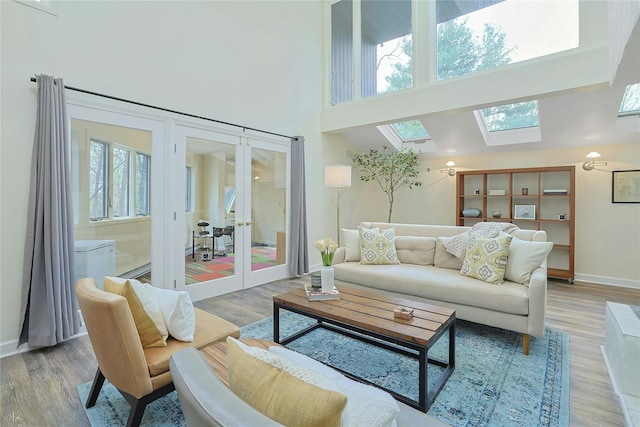 living room with light wood-style floors, a skylight, french doors, and a towering ceiling