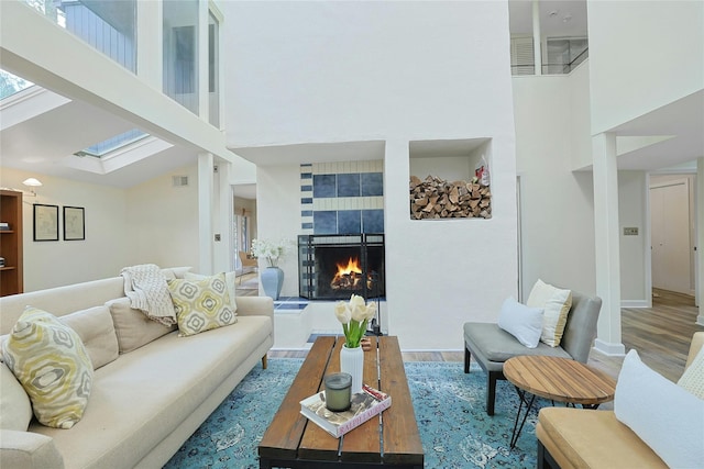 living area with a high ceiling, a skylight, and wood finished floors