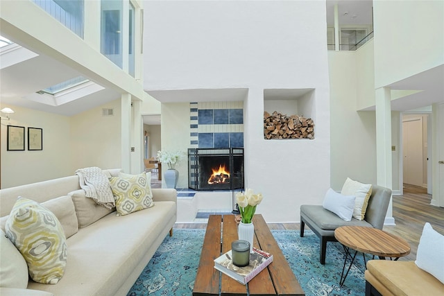 living area featuring visible vents, a towering ceiling, wood finished floors, a fireplace, and a skylight