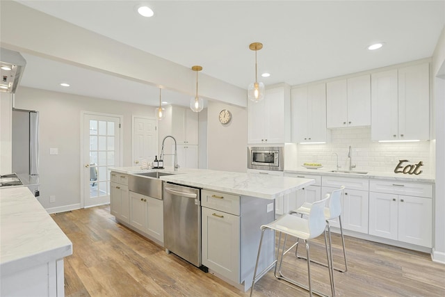 kitchen with appliances with stainless steel finishes, a sink, light wood finished floors, and tasteful backsplash