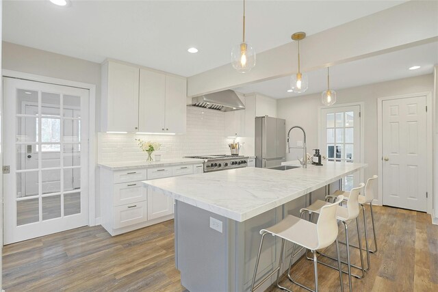 kitchen featuring a kitchen breakfast bar, wall chimney range hood, tasteful backsplash, a sink, and range