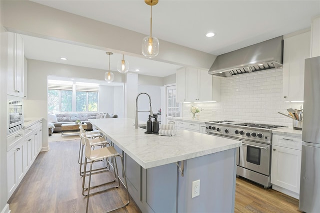 kitchen featuring wall chimney range hood, white cabinets, appliances with stainless steel finishes, open floor plan, and backsplash