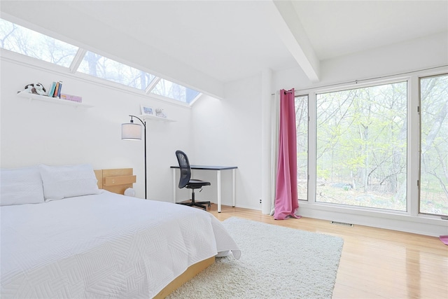 bedroom with a skylight, multiple windows, beam ceiling, and light wood finished floors
