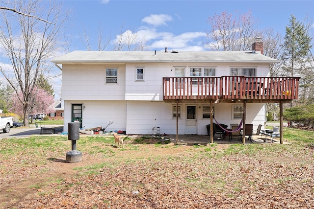 back of house with a patio area, a wooden deck, and a chimney
