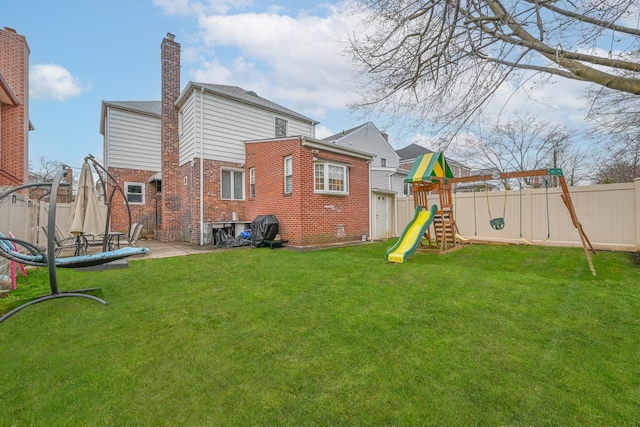rear view of property featuring brick siding, a fenced backyard, a patio, a lawn, and a playground