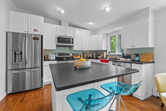 57 Hamilton Dr, Chappaqua, NY 10514 - kitchen featuring appliances with stainless steel finishes, dark countertops, a sink, a kitchen breakfast bar, and white cabinets
