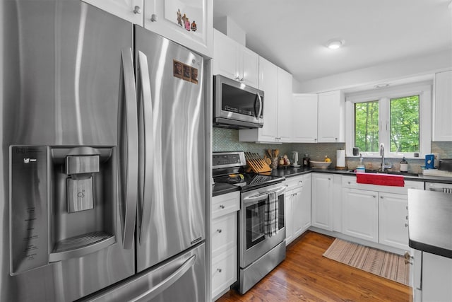 57 Hamilton Dr, Chappaqua, NY 10514 - kitchen featuring stainless steel appliances, dark countertops, white cabinets, decorative backsplash, and a sink